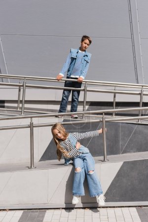 gut gekleidete Kinder in lässiger Jeans-Kleidung posieren in der Nähe von Metallgeländern neben dem Gebäude 