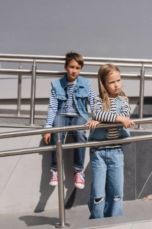 Foto de Well dressed children in casual denim attire posing near metallic handrails next to building - Imagen libre de derechos
