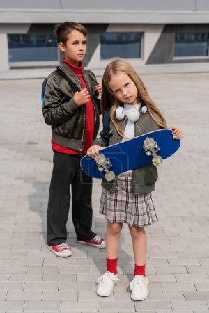 Preteen-Kids in trendigen Bomberjacken stehen mit Penny-Board im Freien 