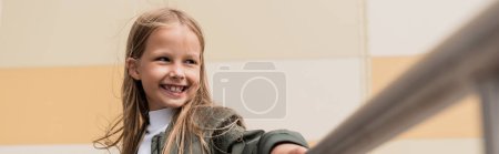 joyeuse fille préadolescente dans une veste de bombardier élégant appuyé sur la main courante métallique près du centre commercial, bannière  
