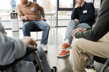 Cropped view of people sitting in circle during alcoholics meeting in rehab center 