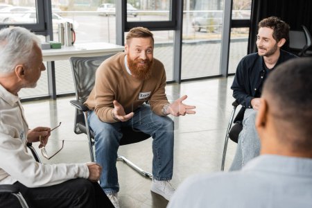 Cheerful man with alcohol addiction talking to interracial group in rehab center 