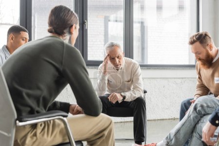 Upset mature man with alcohol addiction sitting in circle during therapy in rehab center 