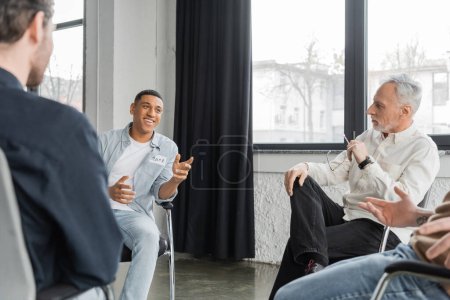 Foto de Hombre afroamericano alegre con adicción al alcohol hablando durante la sesión de terapia de grupo en el centro de rehabilitación - Imagen libre de derechos