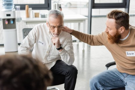 Man calming mature person with alcohol addiction during group therapy session in rehab center 