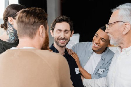 Positive multiethnische Gruppe unterstützt lächelnden Mann bei Alkoholikertreffen im Reha-Zentrum 