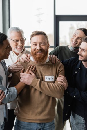 Positive multiethnic people hugging man during alcoholics group therapy in rehab center 