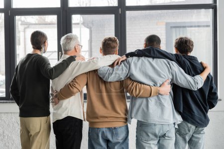 Back view of interracial men with alcohol addiction hugging in rehab center 