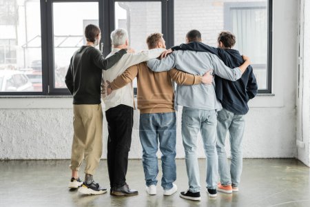Back view of interracial men hugging during anonymous alcoholics meeting in rehab center 