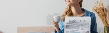 Foto de Vista recortada de la joven satisfecha sosteniendo el periódico de la vida de viaje y la taza de café en el dormitorio, pancarta - Imagen libre de derechos