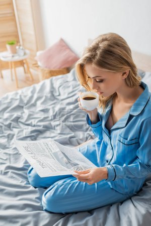 Photo for Blonde woman reading travel life newspaper and drinking coffee in bedroom - Royalty Free Image