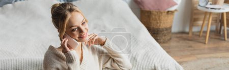 happy woman in knitted sweater talking on smartphone in modern bedroom, banner  