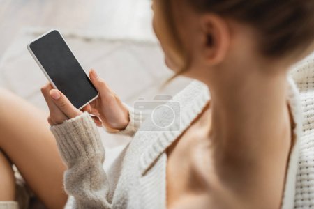 Ansicht der blonden Frau im kuscheligen Pullover per Smartphone mit leerem Bildschirm 