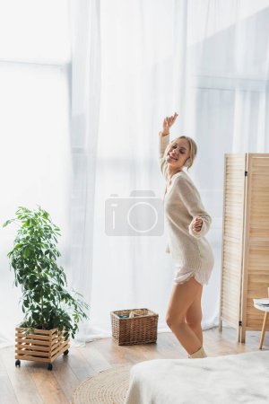 pleased young woman in wireless headphones dancing while having fun in modern apartment 