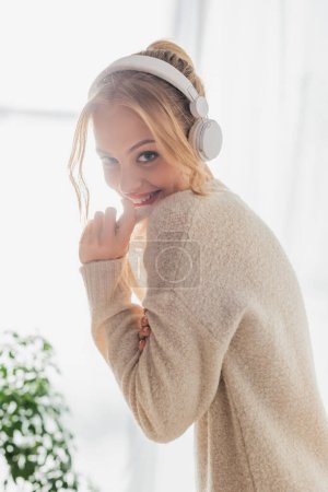 fröhliche junge Frau hört Musik in drahtlosen Kopfhörern, während sie zu Hause Spaß hat 