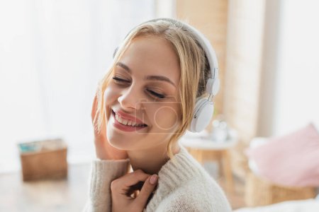 overjoyed young woman listening music in wireless headphones while smiling with closed eyes 