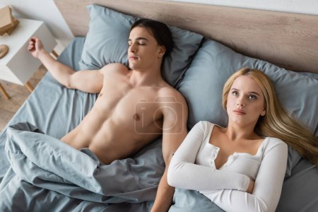 high angle view of embarrassed woman waking up with shirtless man after one night stand 