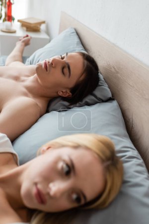 Foto de Shirtless hombre durmiendo cerca avergonzado borrosa mujer después de una noche stand - Imagen libre de derechos