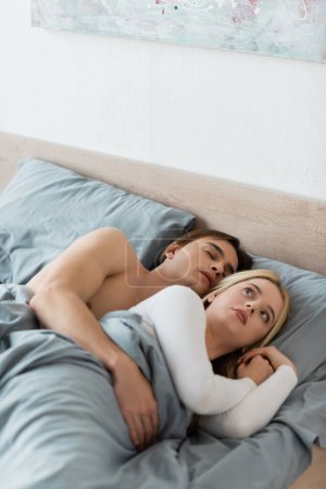 confused woman lying in bed with sleeping man after one night stand 