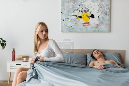 blonde woman pulling blanket while shirtless man sleeping after one night stand  