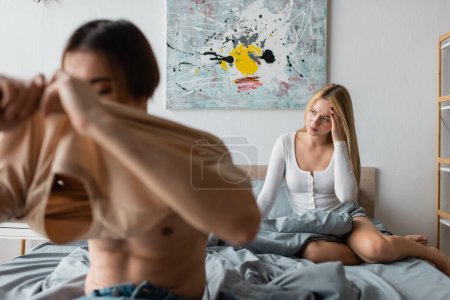 blonde woman feeling headache and regretting of having one night stand with man on blurred foreground 