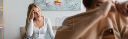 blonde woman having headache and regretting of having one night stand with man on blurred foreground, banner 