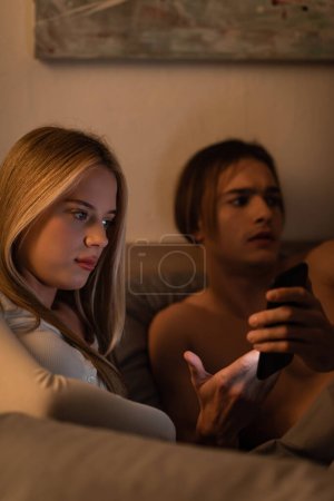 Foto de Hombre sin camisa mostrando teléfono inteligente a novia infiel en el dormitorio - Imagen libre de derechos