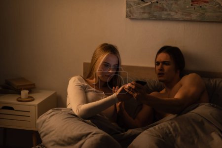 Téléchargez les photos : Jeune femme lisant des messages sur smartphone du petit ami inquiet la nuit, concept de tricherie - en image libre de droit