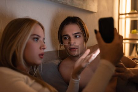 Foto de Mujer rubia sosteniendo el teléfono móvil mientras discute con el novio en el dormitorio, concepto de engaño - Imagen libre de derechos