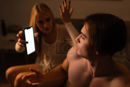Photo for Blonde woman holding smartphone while arguing with unfaithful boyfriend at night - Royalty Free Image