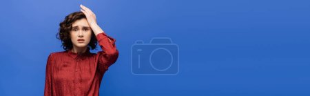Photo for Stressed language teacher touching head while looking at camera isolated on blue, banner - Royalty Free Image