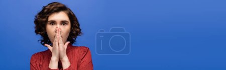 Photo for Shocked language teacher covering mouth with hands while looking at camera isolated on blue, banner - Royalty Free Image