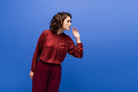 curious language teacher in maroon color outfit looking down isolated on blue 