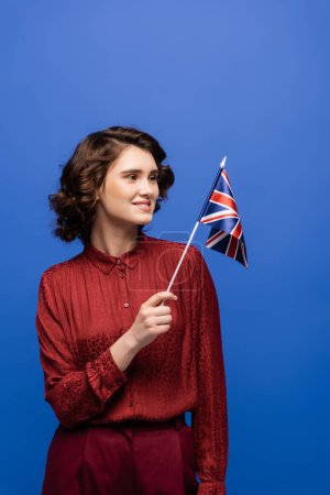 happy language teacher smiling while looking at flag of United Kingdom isolated on blue 
