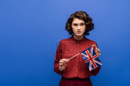 serious language teacher holding flag of United Kingdom isolated on blue 