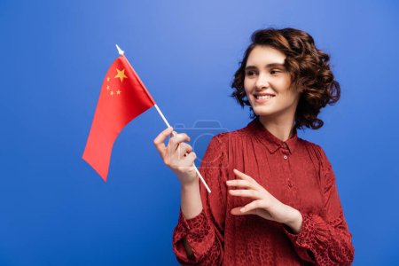 happy language teacher smiling while holding flag of China isolated on blue 