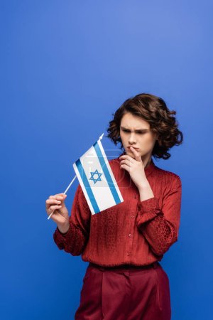 pensive woman with curly hair holding flag of Israel isolated on blue  