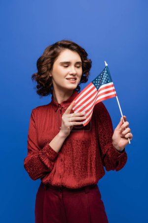 positive language teacher smiling while looking at usa flag isolated on blue