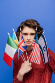 confident and young student with different international flags looking at camera isolated on blue t-shirt #645932154