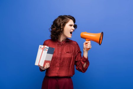 angry language teacher holding textbooks and screaming in megaphone isolated on blue