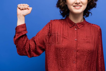 Téléchargez les photos : Vue recadrée du professeur de langue des signes souriant montrant le geste de puissance isolé sur bleu - en image libre de droit