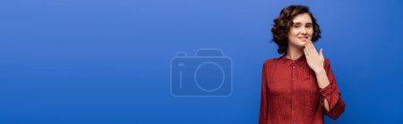 Téléchargez les photos : Femme gaie en chemisier rouge dire merci sur le langage des signes isolé sur bleu, bannière - en image libre de droit