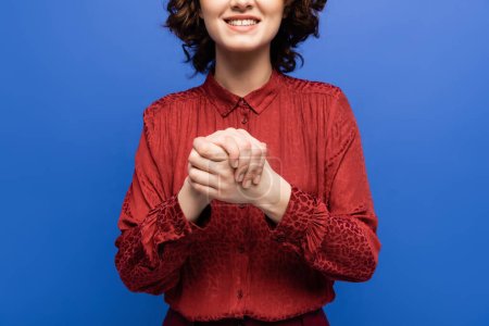 partial view of smiling teacher showing symbol meaning friendship on sign language isolated on blue