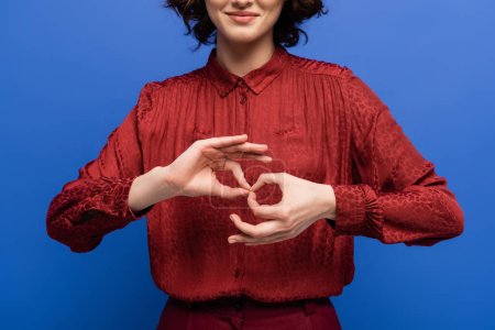 Ausgeschnittene Ansicht einer positiven Frau, die Geste zeigt, die Dolmetscher bedeutet, auf Zeichensprache isoliert auf blau