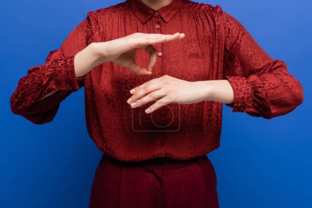 abgeschnittene Ansicht einer Frau in roter Bluse, die über Gebärdensprache spricht, isoliert auf blauem Grund