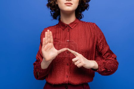 partial view of teacher in burgundy blouse using sign language isolated on blue