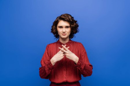Photo for Young teacher looking at camera and showing gesture in sign language isolated on blue - Royalty Free Image