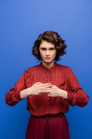 Téléchargez les photos : Jeune femme aux cheveux bouclés montrant signe signifiant nom sur langage des signes isolé sur bleu - en image libre de droit
