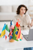 selective focus of international flags near blurred laptop and young language teacher working at home tote bag #645933104