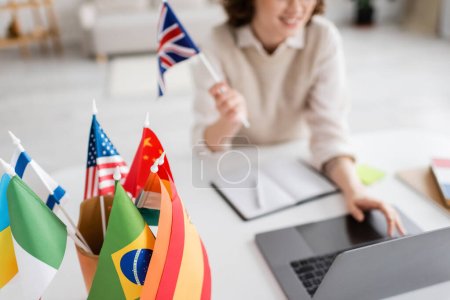 enfoque selectivo de banderas internacionales cerca de profesor de idiomas extranjeros utilizando el ordenador portátil en fondo borroso 